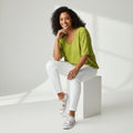 a woman wearing a green shirt and white jeans on a white background