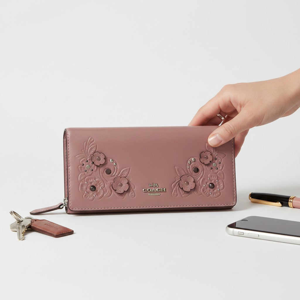 Hand holding a Coach wallet with floral designs on a light background