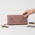 Hand holding a Coach wallet with floral designs on a light background