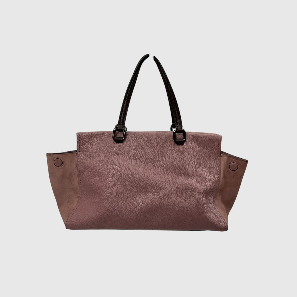 A dusty rose pebbled leather tote bag with black shoulder straps and side pockets, shown against a light gray background.