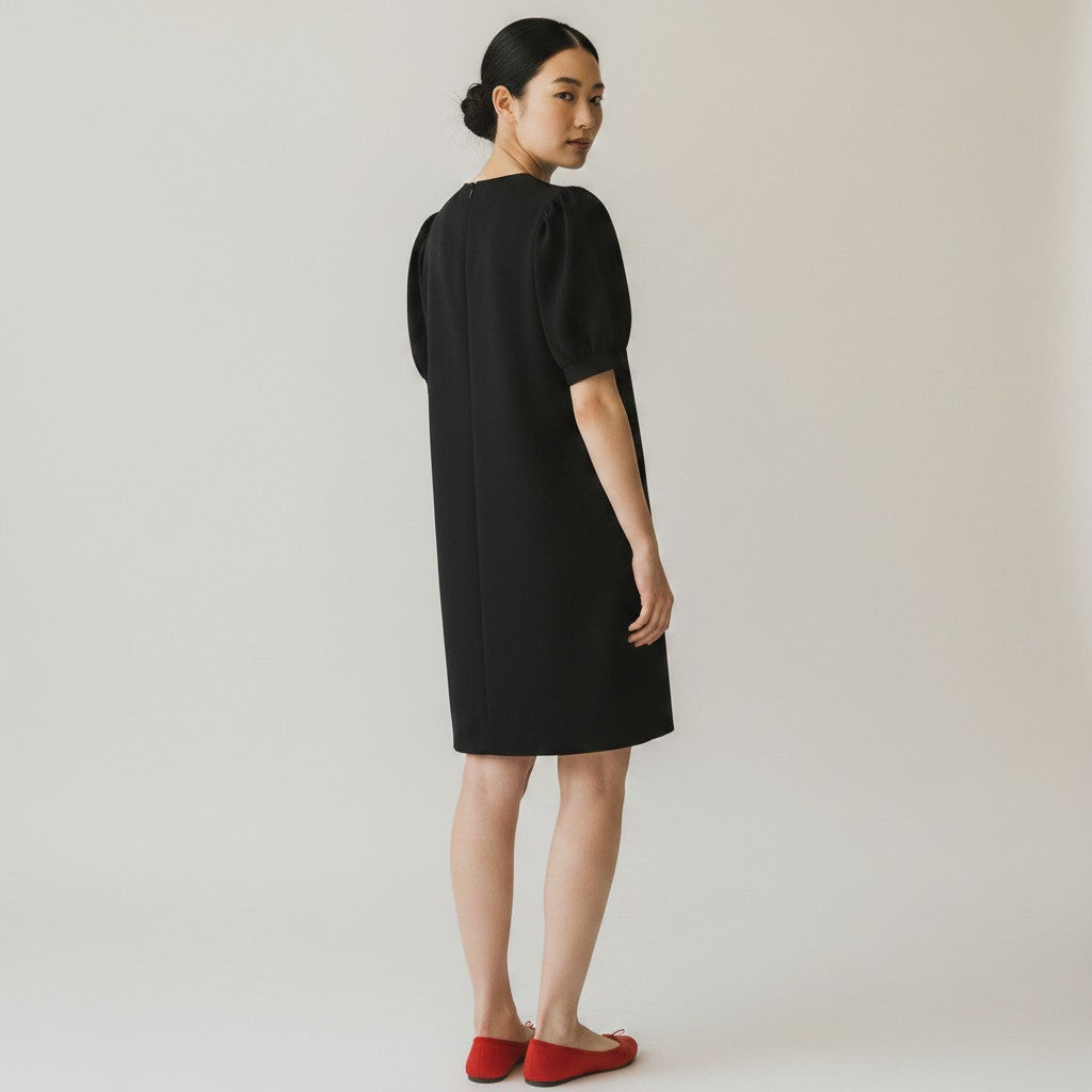 Woman wearing a black dress with puff sleeves on a plain background