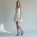 Woman wearing a white dress with blue high heels against a plain background