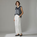 Woman wearing a navy floral top and white pants against a gray background