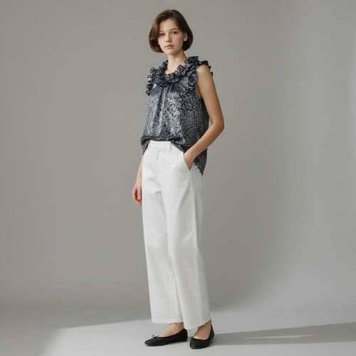 Woman wearing a navy floral top and white pants against a gray background