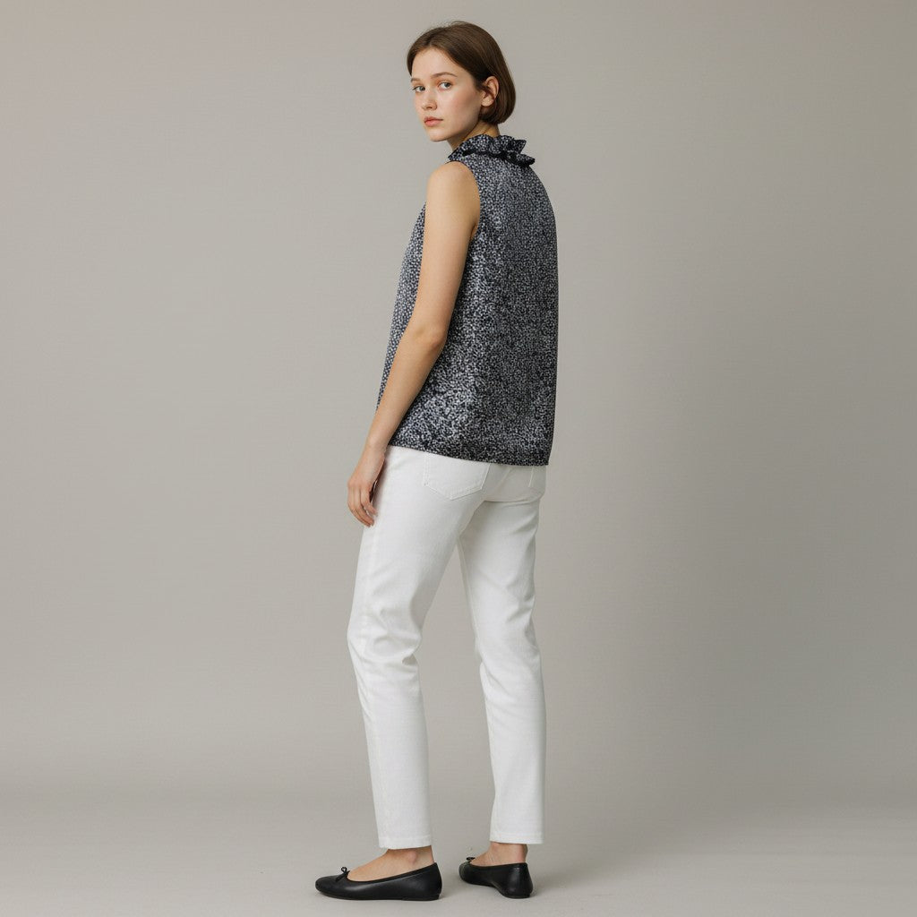 Woman wearing a sleeveless patterned top and white pants on a plain background