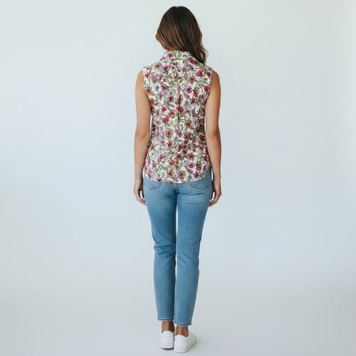 Woman wearing a sleeveless floral top and blue jeans on a white background