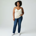 Woman wearing a white tank top and blue jeans on a plain background