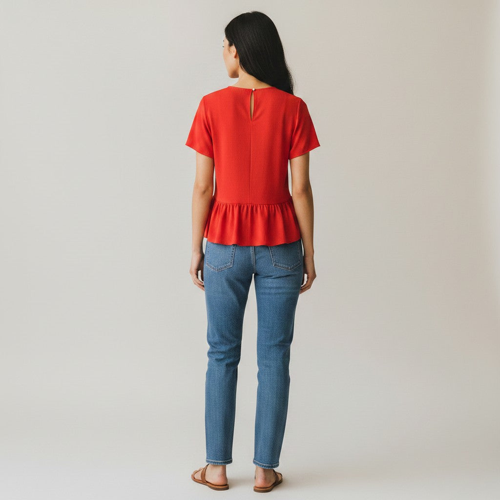 Woman wearing a red peplum top and blue jeans on a plain background