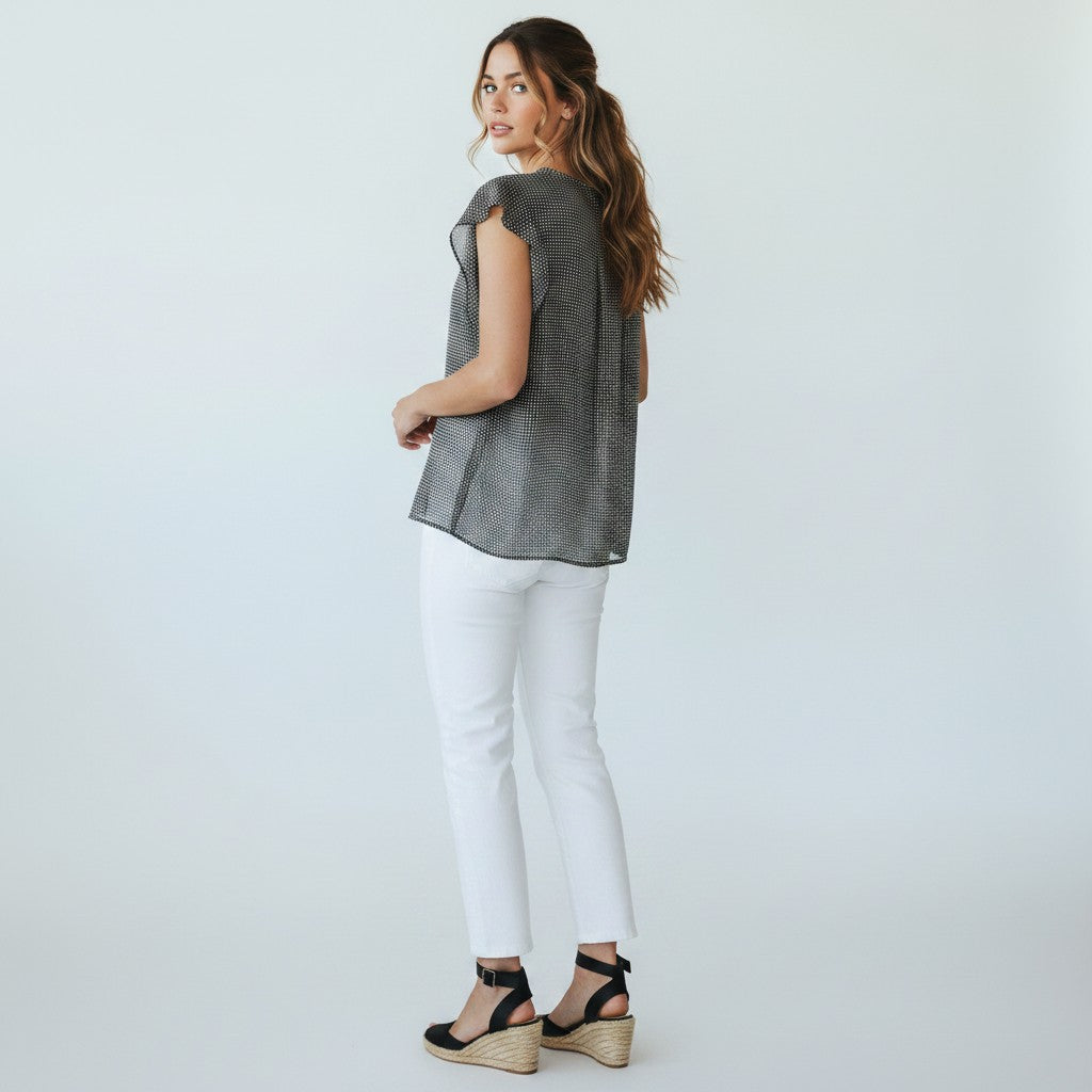 Woman wearing a sleeveless patterned top and white pants on a plain background