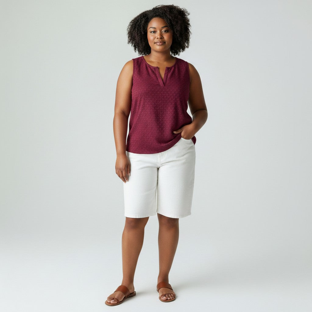 Woman wearing a maroon sleeveless top and white shorts on a plain background