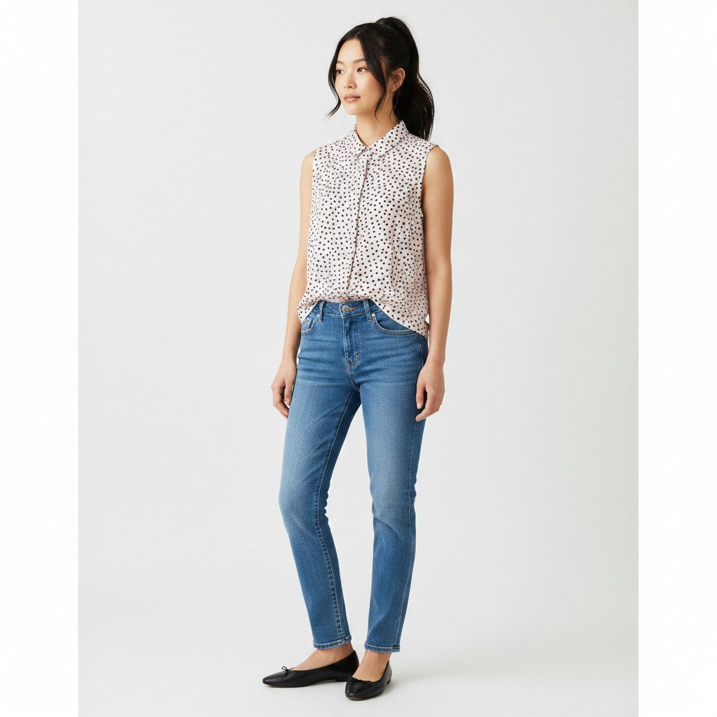 Woman wearing a sleeveless polka dot blouse and blue jeans on a white background