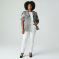 Woman wearing a black and white checkered jacket with white pants on a plain background