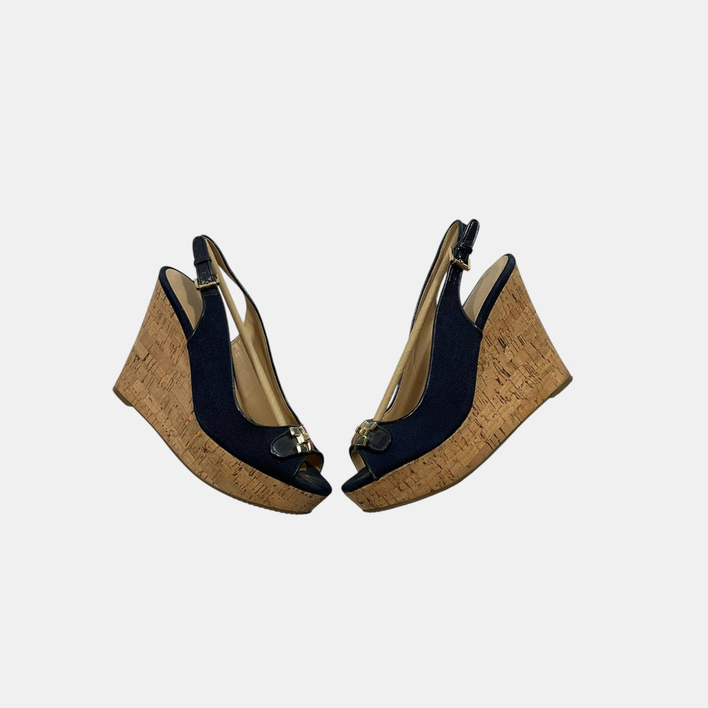Pair of wedge sandals with cork wedge and black upper on a light gray background