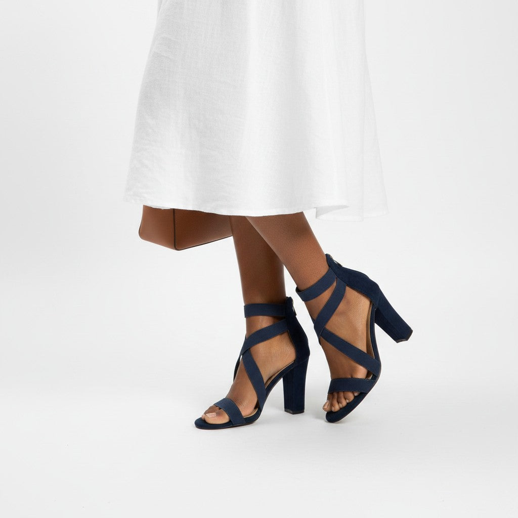 Navy high-heeled sandals worn with a white dress on a white background