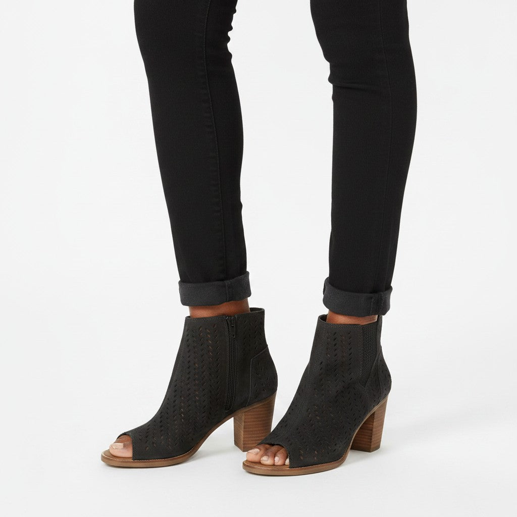Black open-toe ankle boots worn with black jeans on a white background