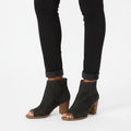 Black open-toe ankle boots worn with black jeans on a white background