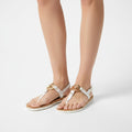 White sandals with gold accents worn by a person on a light gray background