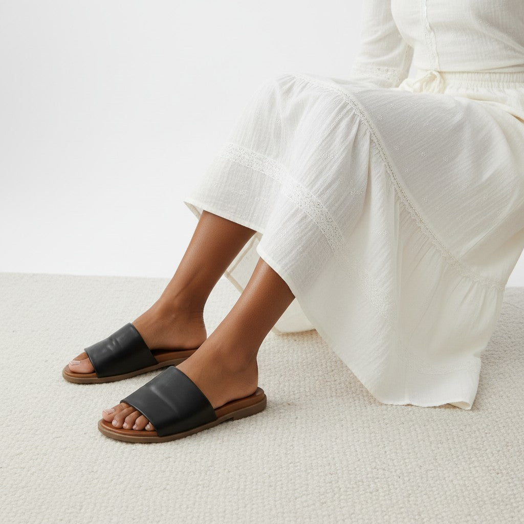 Person wearing black sandals and white pants on a light background