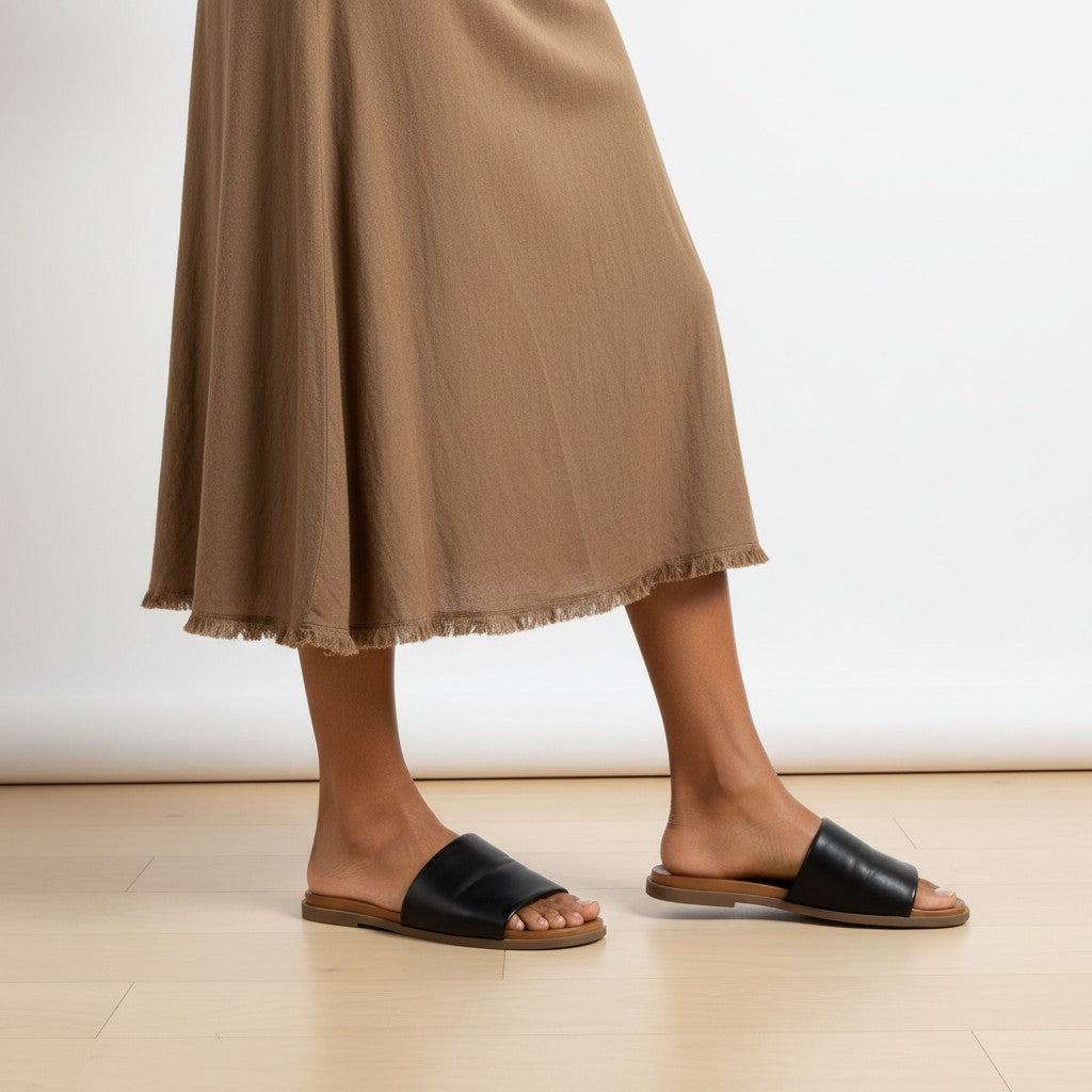 Person wearing black sandals and a brown skirt on a light wooden floor.