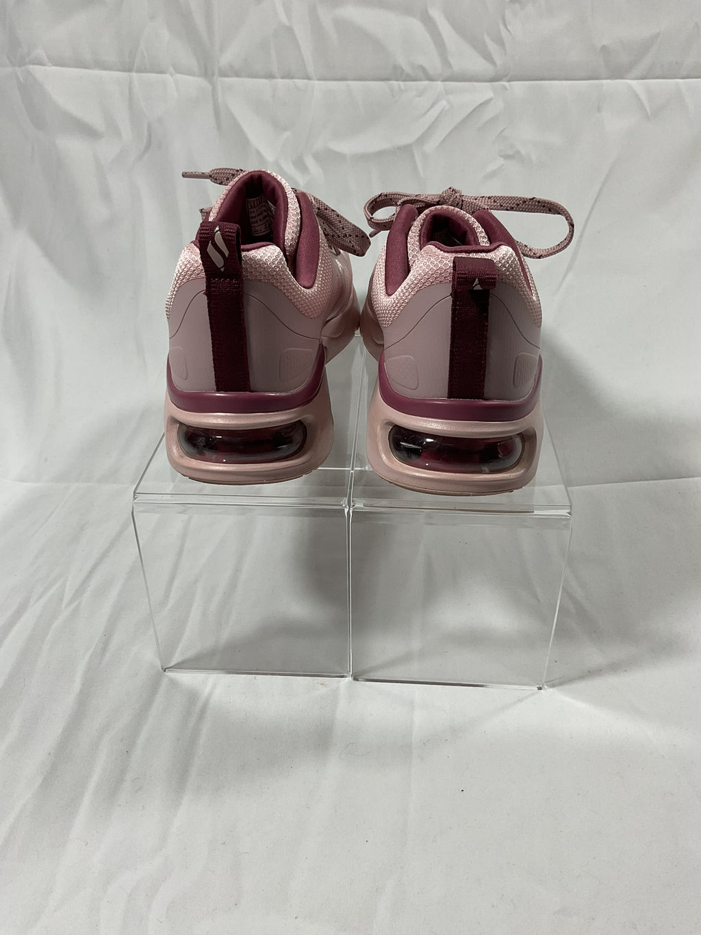Pink sneakers on a clear stand against a white background