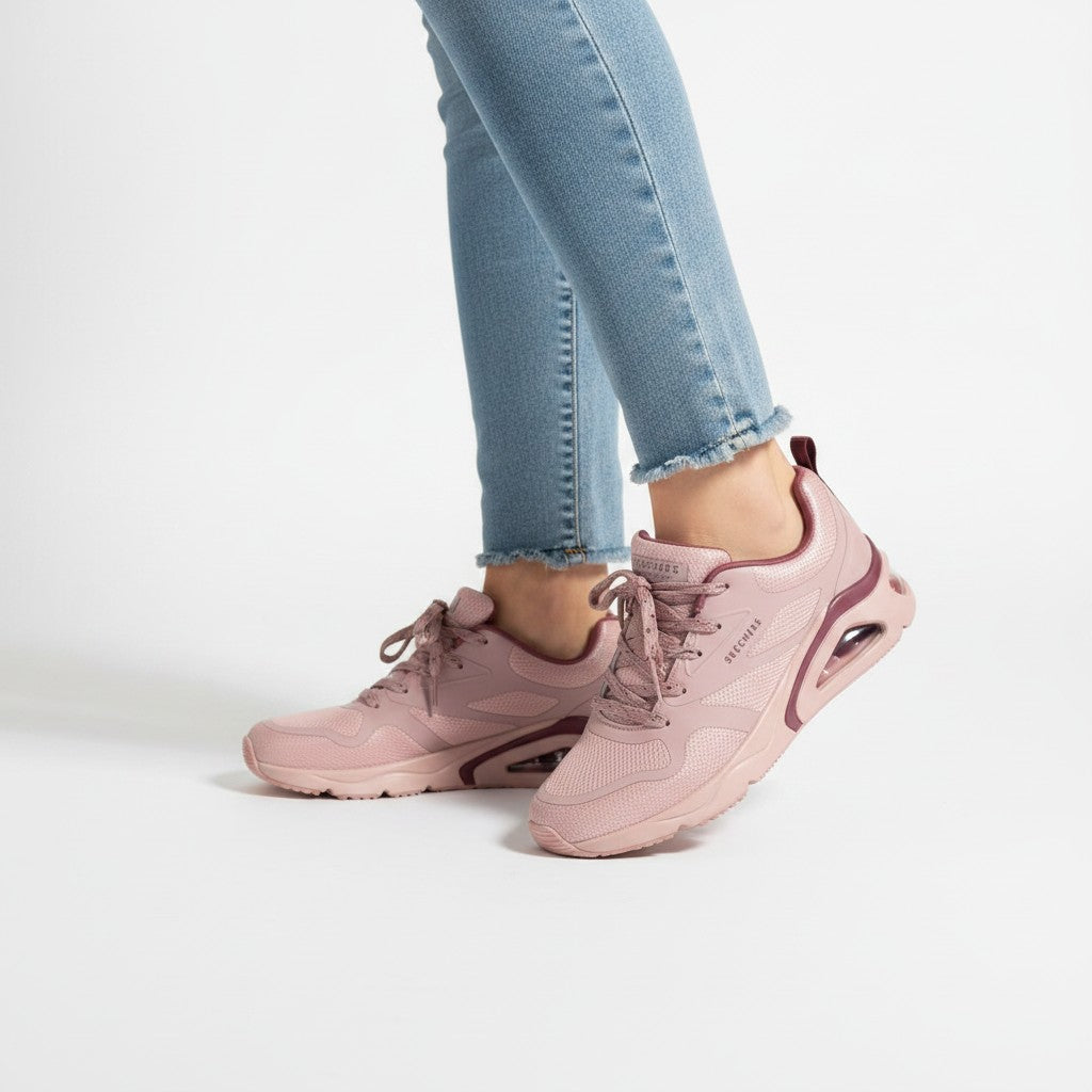 Pink sneakers worn with light blue jeans on a white background