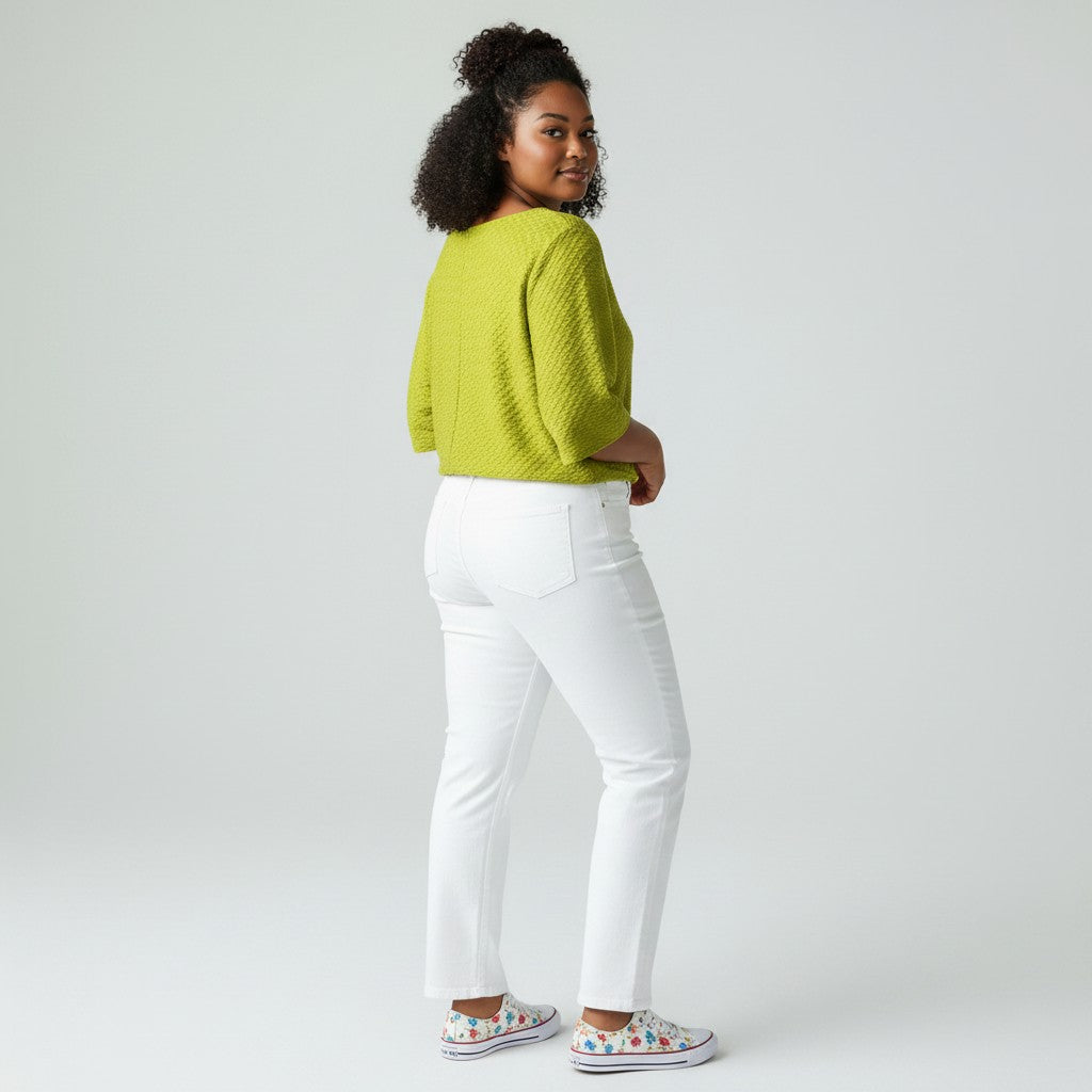 A woman wearing a textured lime green knit sweater and white pants, photographed from the back in a studio setting.