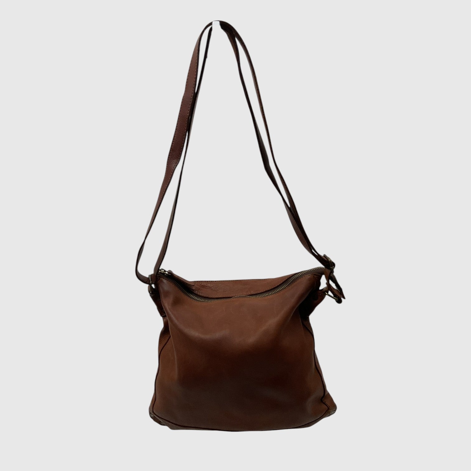 A brown leather shoulder bag with a long adjustable strap, photographed against a solid light gray background.