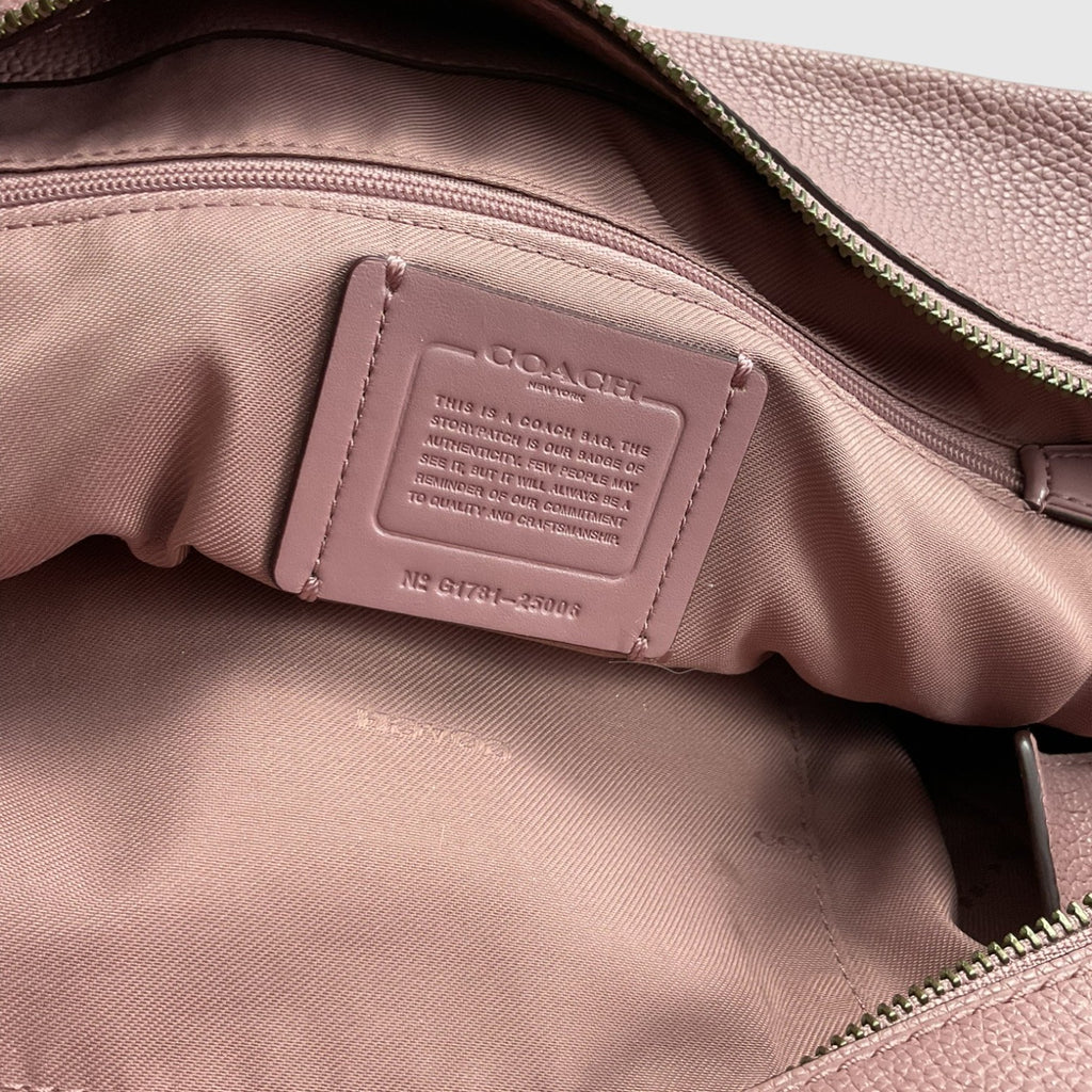 Close-up of the interior of a Coach bag in dusty pink pebbled leather, showing a matching pink interior lining with a stitched Coach label and zipper details.