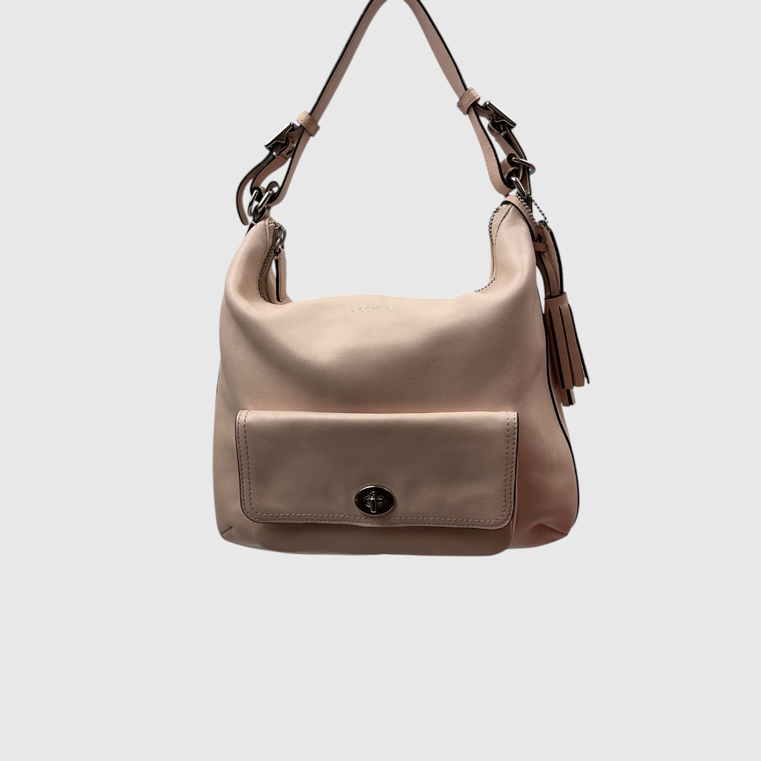 A light beige leather shoulder bag with a front flap pocket and a dark metal turn-lock closure, shown against a plain light gray background.