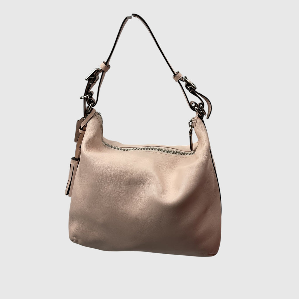 A slouchy shoulder bag in light beige leather with a black strap and silver-tone hardware, shown against a plain light gray background.