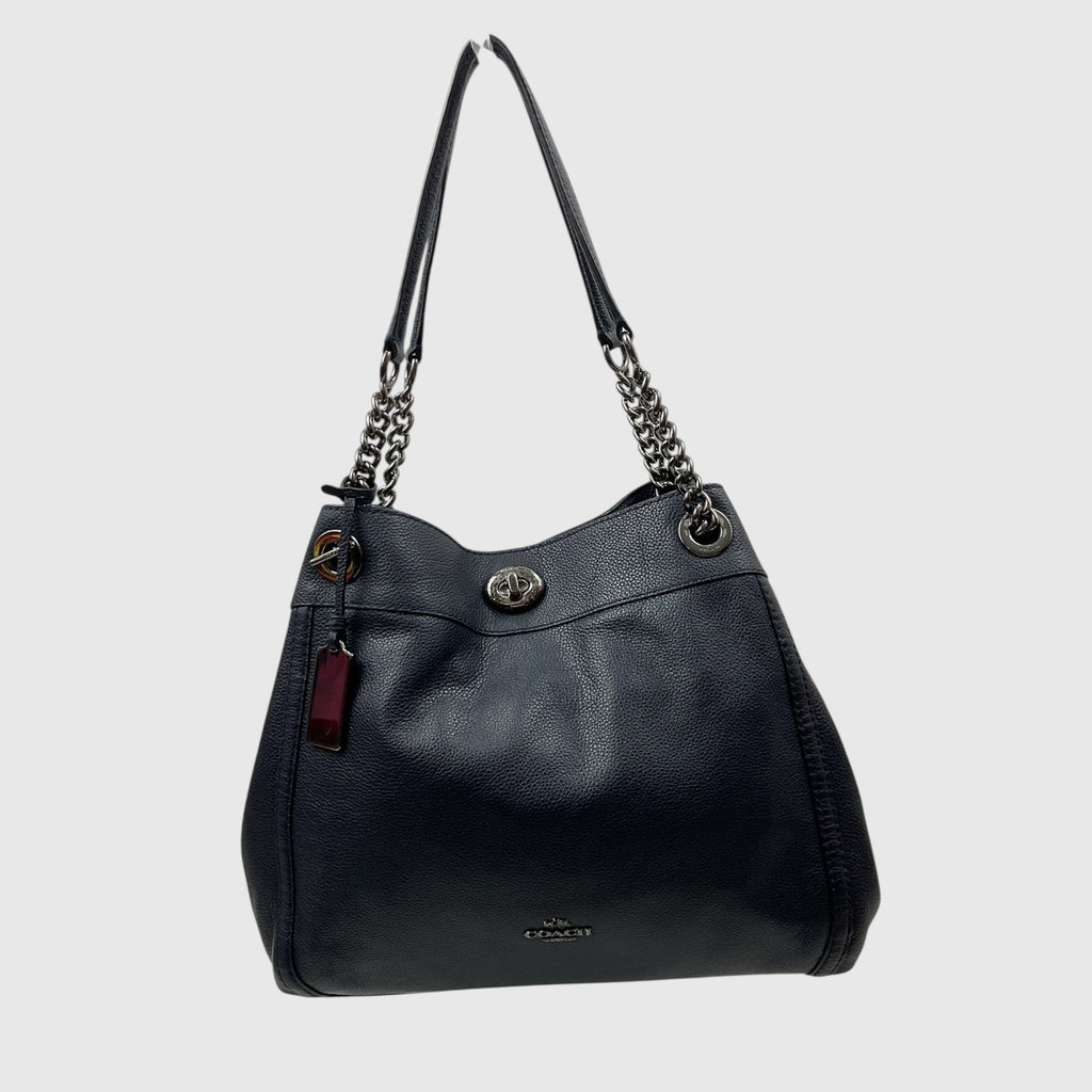 A Coach black pebbled leather hobo shoulder bag with silver-tone chain strap details and a small red leather hangtag, shown against a light gray background.