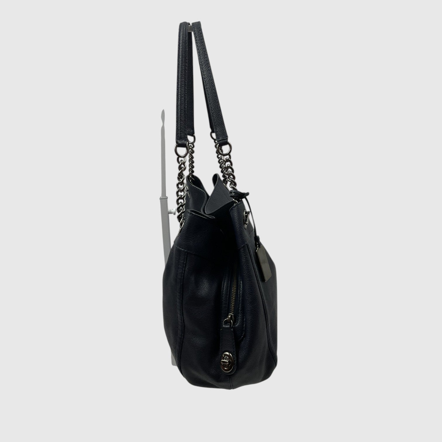 A black leather shoulder bag with a top handle, a detachable chain strap, and a zippered pocket, shown from a side profile view against a light gray background.