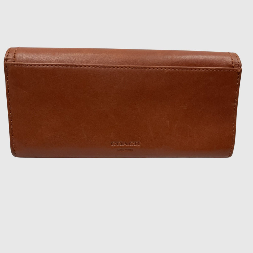 A brown leather wallet with a subtle embossed Coach logo on the front, photographed against a light gray background.