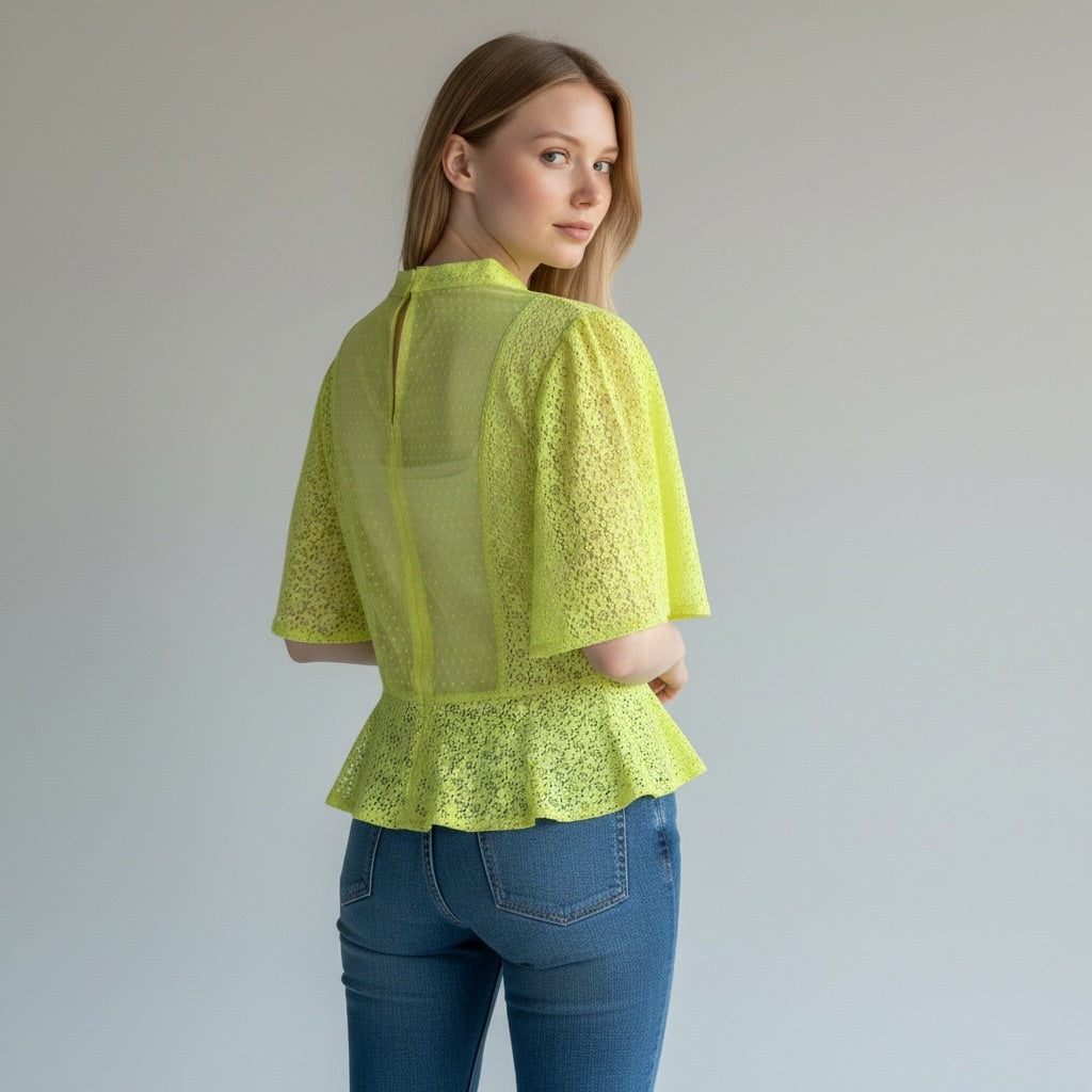 Woman wearing a bright green lace top and blue jeans against a plain background