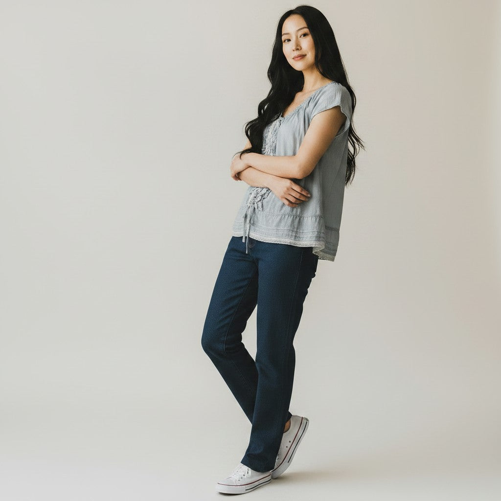 Woman wearing a gray sleeveless top and dark blue jeans with white sneakers on a plain background