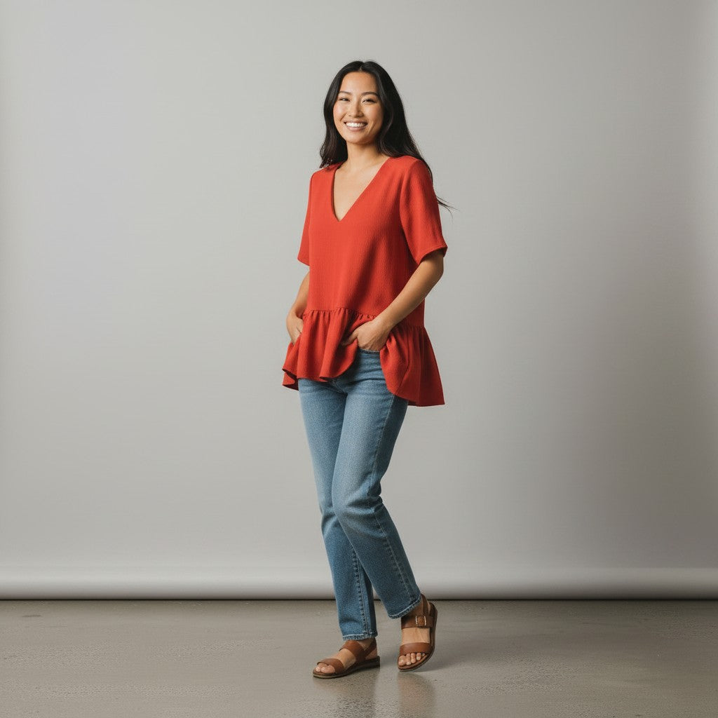 Woman wearing a red blouse and blue jeans standing against a plain background
