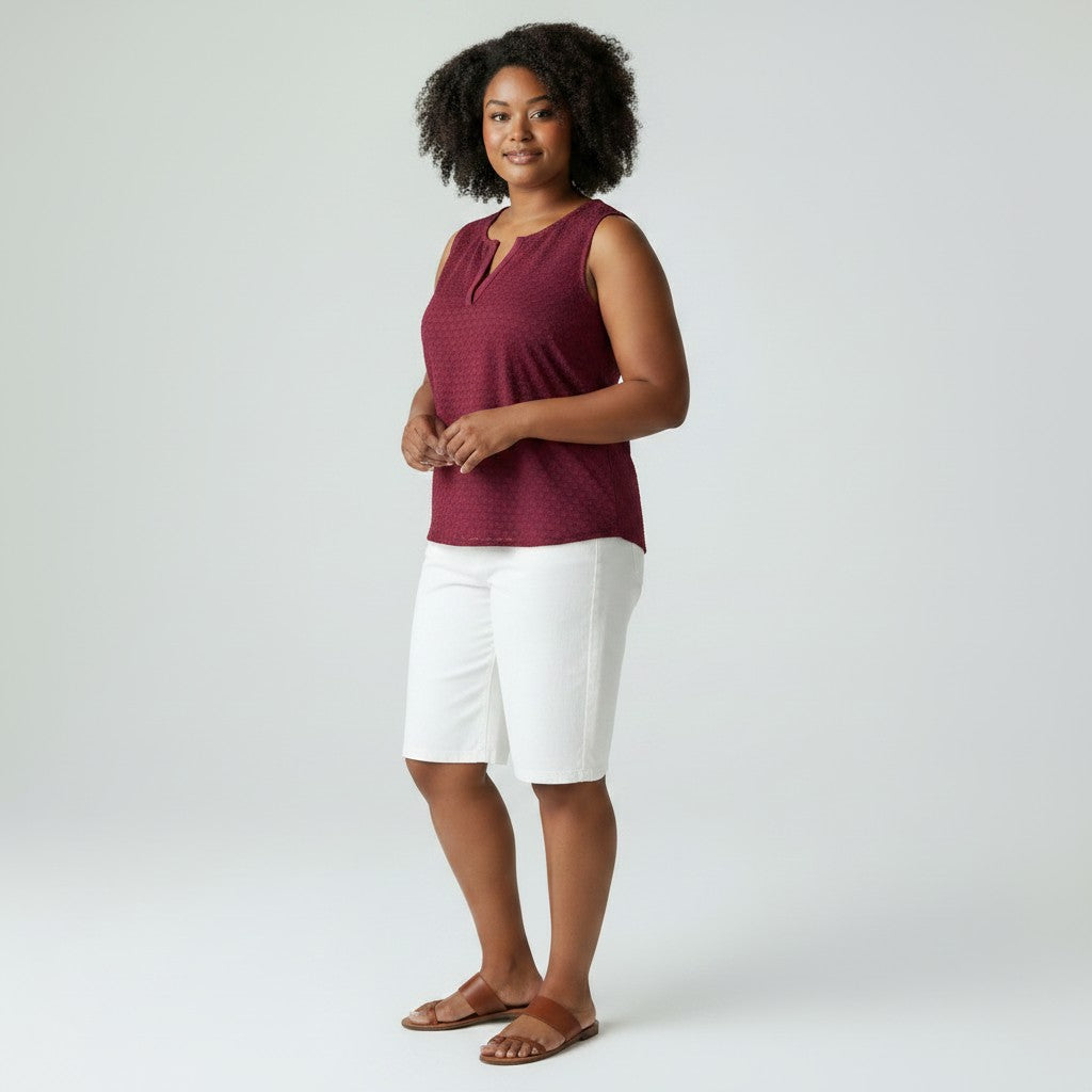 Woman wearing a maroon sleeveless top and white shorts on a plain background