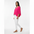 Woman wearing a bright pink top and white pants on a white background