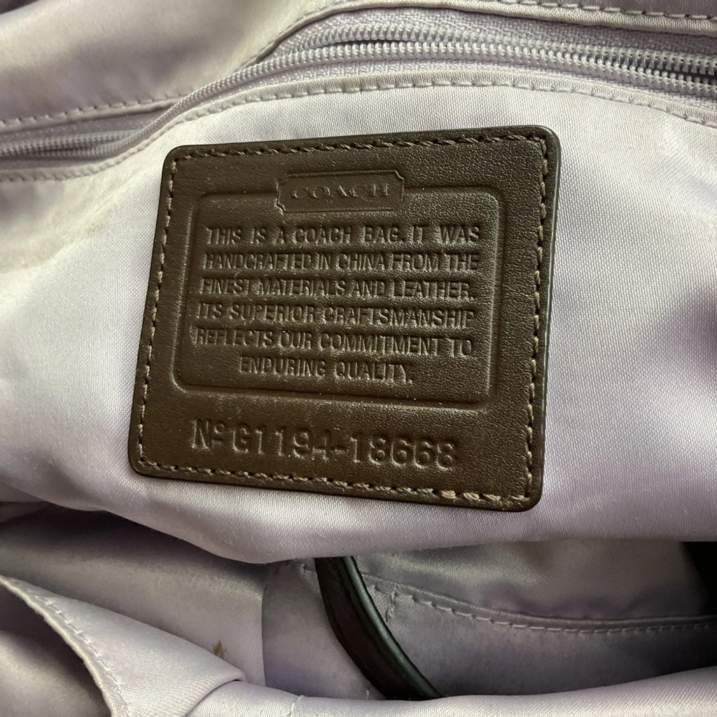Close-up of an interior Coach bag patch showing embossed text on a light gray fabric background.